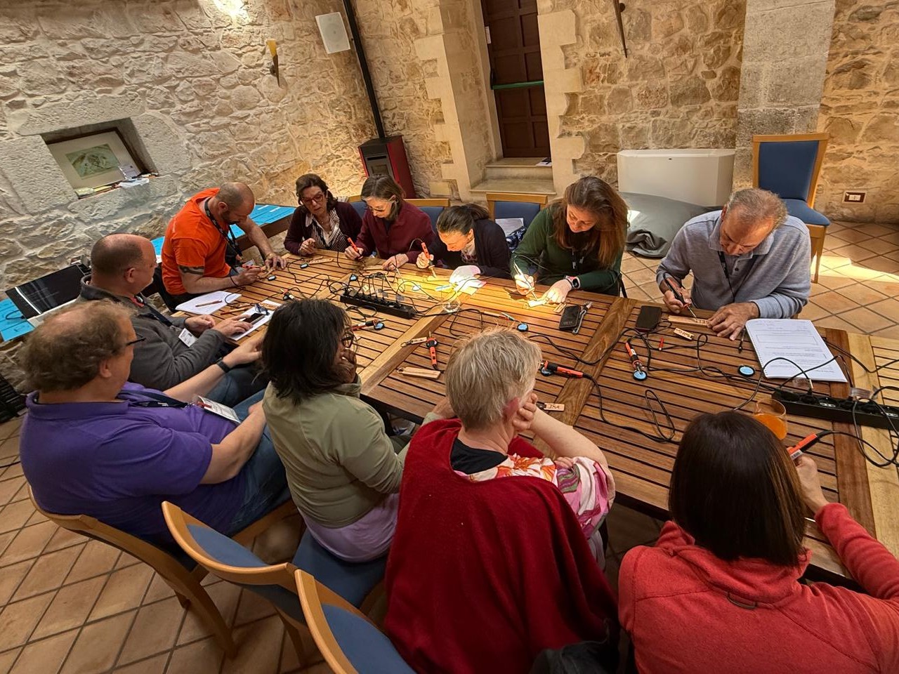 Retreat participants making candles together around a long wooden table in a stone-walled room
